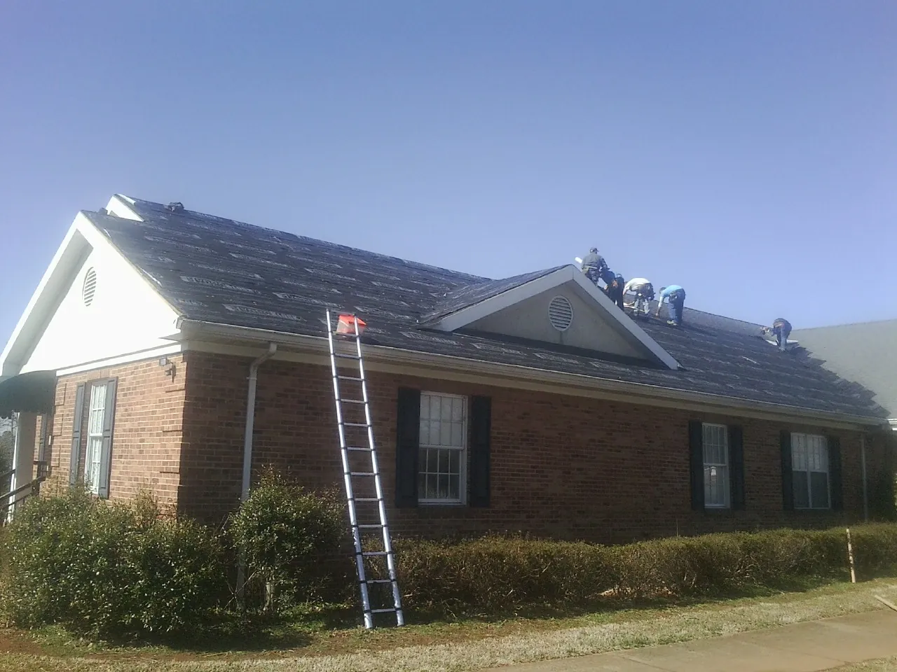 Crew tearing shingles off a brick ranch roof with a ladder set — Metal Roof Repair work by our crew in Juniata