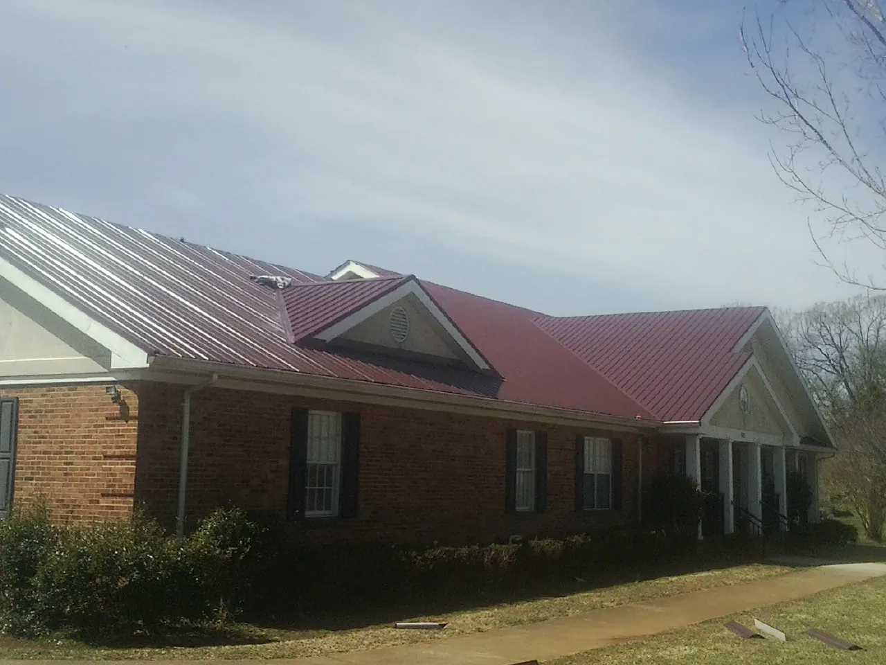 Red metal roof with gabled entries on a long brick building, from a Hail Damage Roof Repair job in Juniata