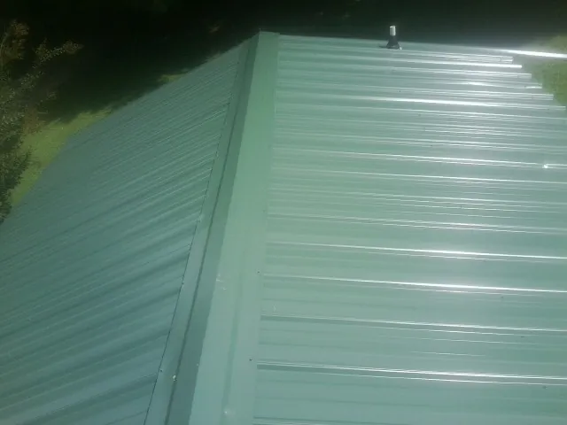 New green metal panels meeting at the ridge of a roof — Flat Roof Repair work by our crew in Juniata