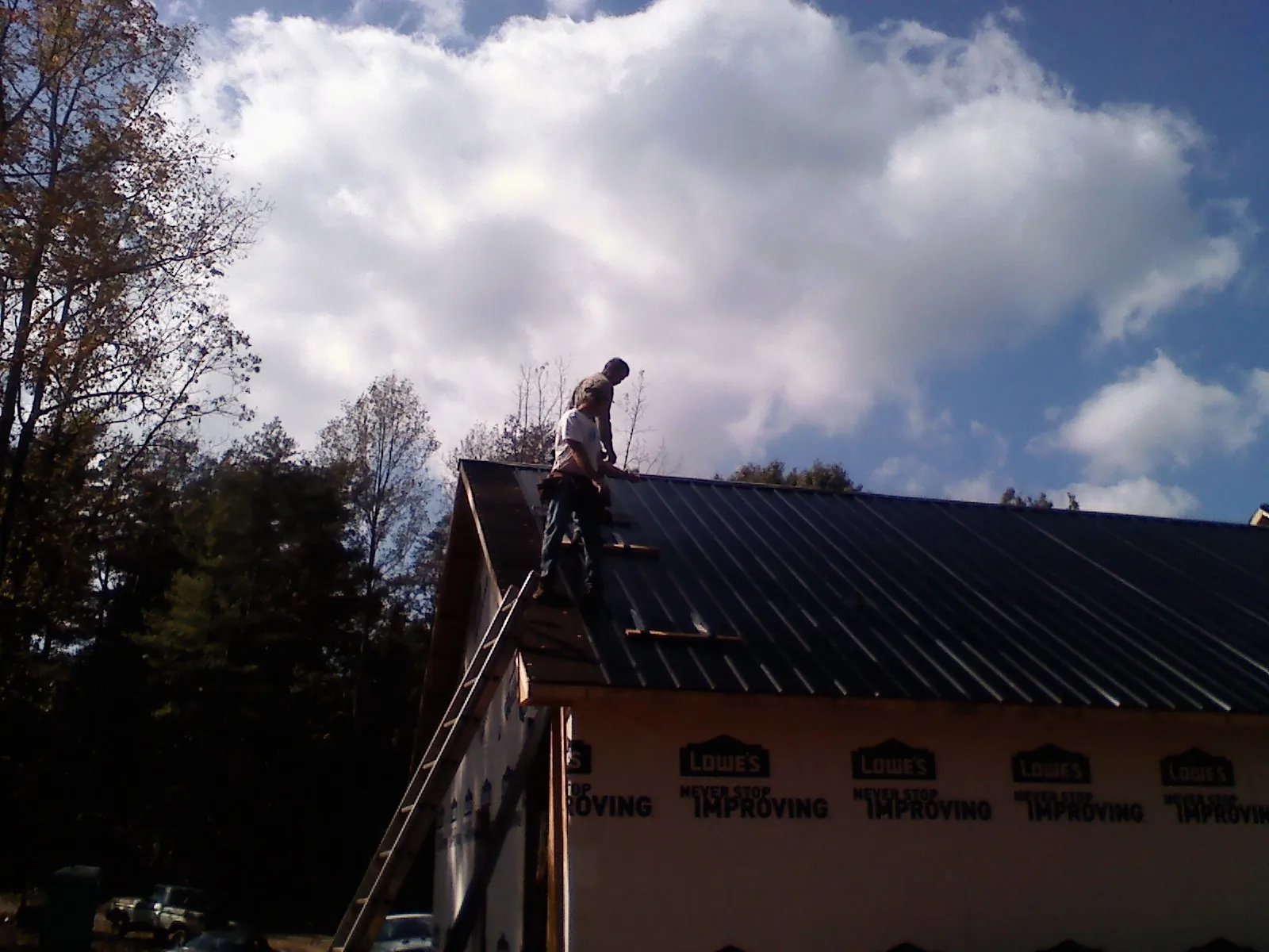 Roofer fastening dark metal panels high against a cloudy sky, from a Roof Inspection job in Juniata
