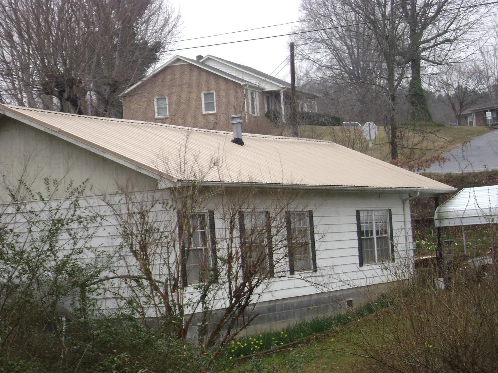 Tan metal roof on a white sided house set into a hillside — Commercial Roofing by Roofing Brothers in Juniata