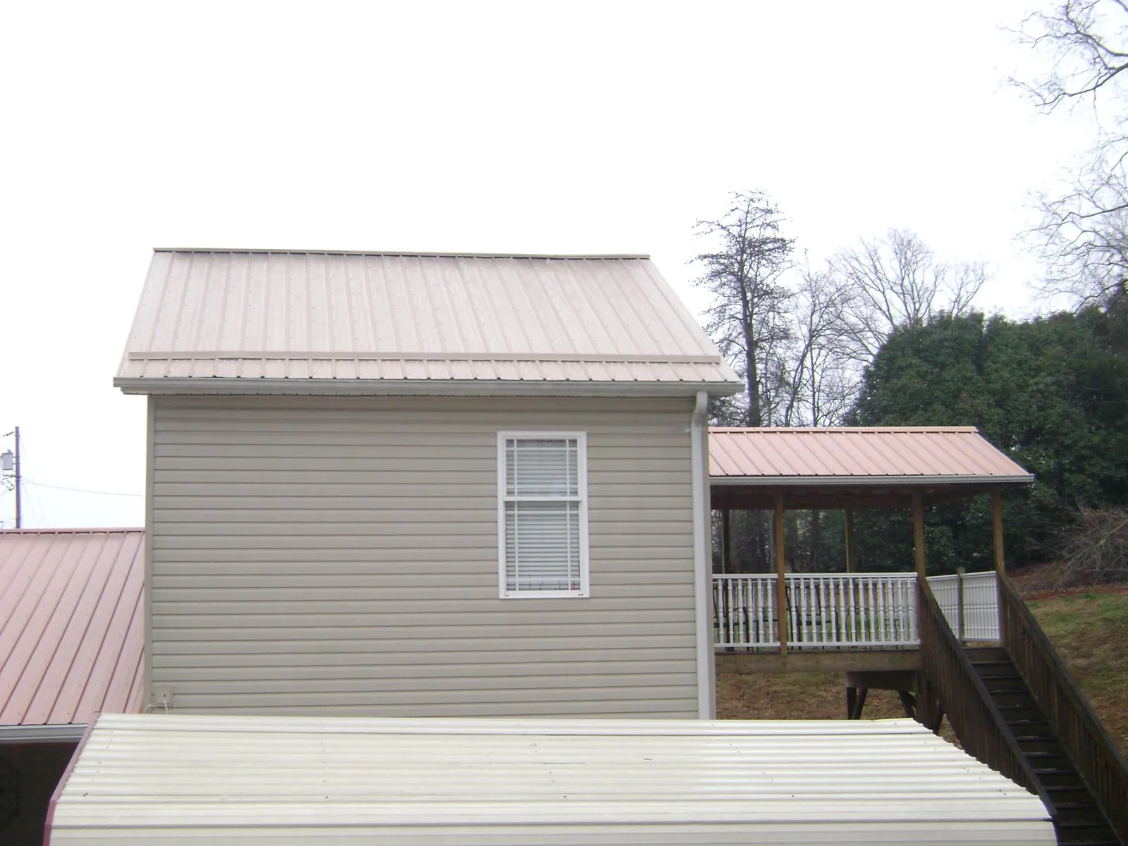 Tan metal roofs on a two story addition and attached porch, from a Roof Replacement job in Juniata
